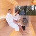 Couple enjoying the Luna Outdoor Sauna 2.3 x 2.4m with drinks and woman using the ladle.