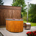 Fiberglass Ofuro Hot Tub with a metal stove, placed on a wooden deck with a garden backdrop.