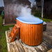 Steaming Fiberglass Ofuro Hot Tub with a blue interior, wooden steps, and a metal stove on a deck.