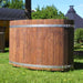 Oval cold tub with a log cabin in the background.