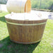 Oval cold tub made from spruce with a wooden lid in lighted green setting.