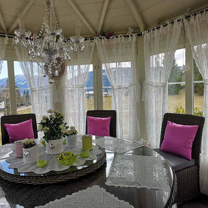 Luxurious interior of the Pavilion 10m² Sun featuring lace curtains, bright pink cushions, a crystal chandelier, and panoramic views of the surrounding landscape.