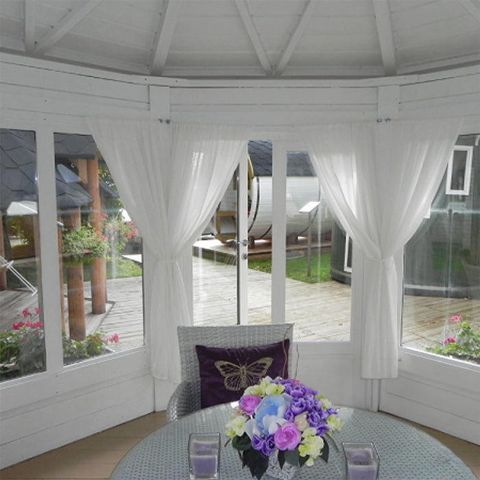 Cosy and bright Pavilion 10m² Sun interior with white curtains, a floral centrepiece, and a stunning garden view through large windows.