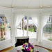 Interior detail of the Pavilion 10m² Sun showing a glass table with floral decorations, surrounded by white wicker chairs and a natural wooden finish.