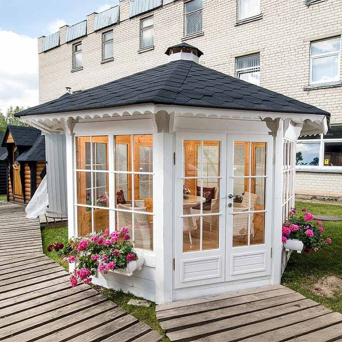 Outdoor setting of the Pavilion 10m² Sun with vibrant pink flowers, a modern white design, and black roof shingles blending seamlessly into the garden.