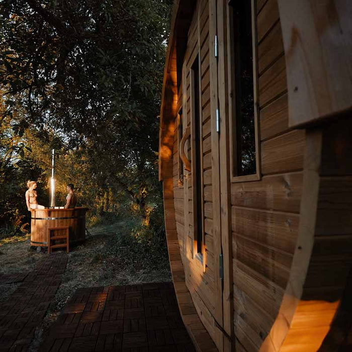 Two persons relaxing next to Traditional Sauna Barrel.