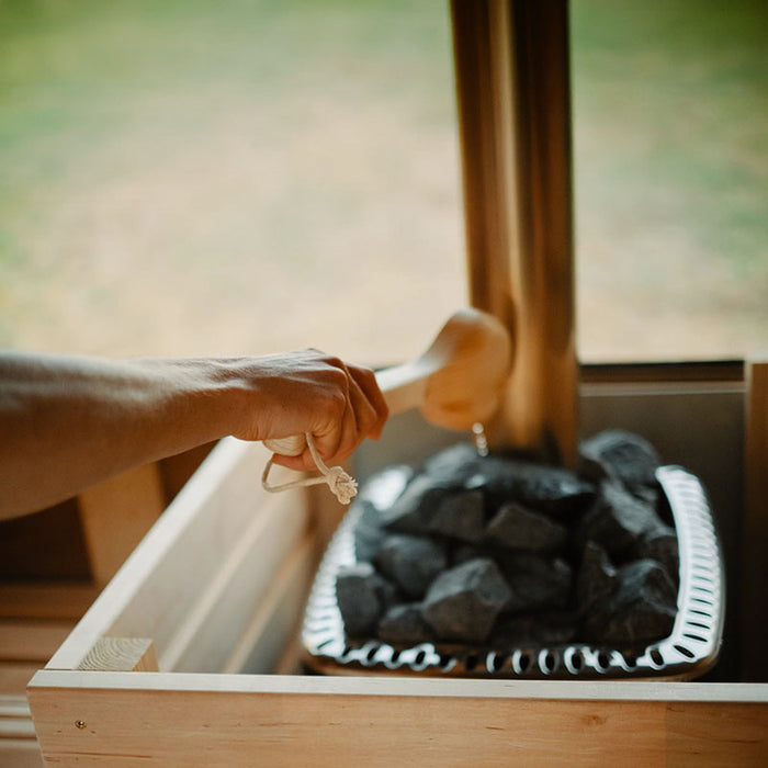 Hand pouring water on sauna rocks inside a wooden sauna.