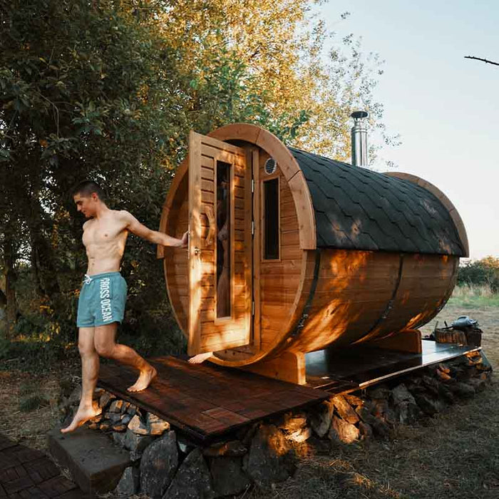 Sauna Barrel 1.9 x 3m a with an open door and chimney, set outdoors with a person about to exit.