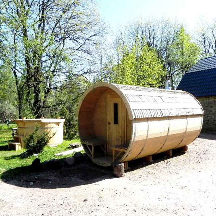 The Traditional Sauna Barrel 2.2 x 4m set in an outdoor environment with green trees and a clear sky.