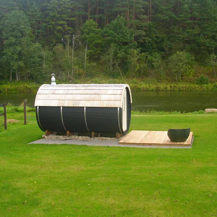 The Traditional Sauna Barrel 2.2 x 4m  placed on a grassy area near a body of water. 