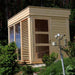 Outdoor traditional sauna cube with glass windows and door, surrounded by greenery.