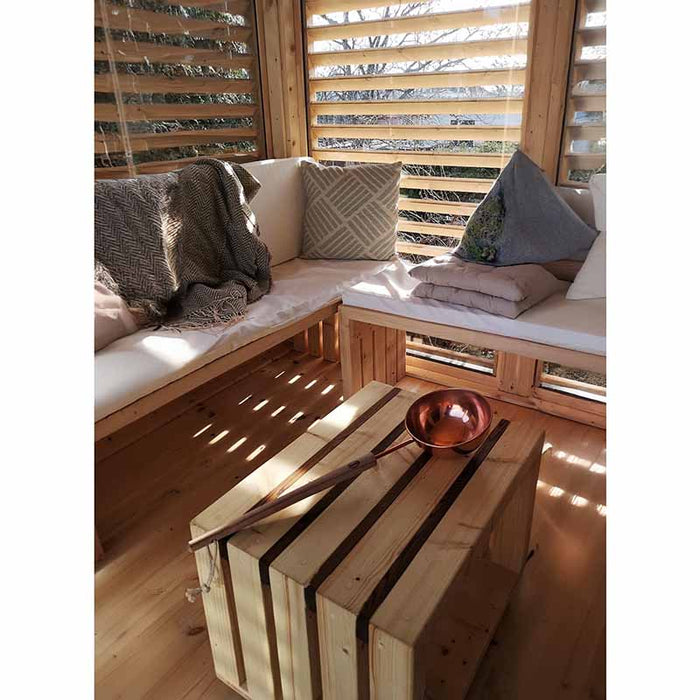 Close up view of wooden table with ladle and wooden benches with pillows in the background. 