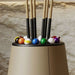 Close-up of the Vismara Bobo Cue Rack showcasing pool cues and vibrant billiard balls in an elegant matte beige finish against a stone wall.