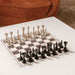 Stylish Vismara Scaccomatto Chess Table setup with black and silver chess pieces, placed in a warm-toned lounge with contemporary cushions and decor.