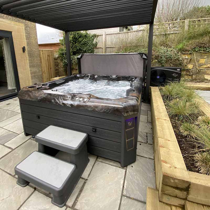 Wellis Valencia 7 Person Hot Tub installed on tiled patio under black pergola, ideal for modern holiday lets and private homes.