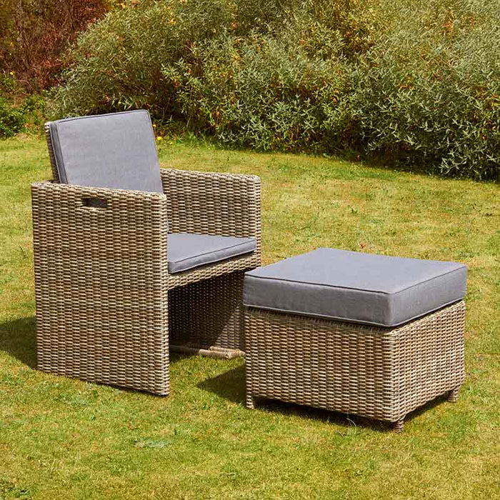 Rattan chair and stool from the Wentworth 10 Seater Cube Dining Set placed on a garden lawn, showcasing the durable outdoor design.