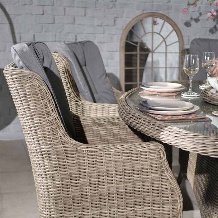 A close-up of a place setting on the glass-top oval table from the Wentworth 6 Seater Ellipse Imperial Dining Set, featuring elegant dinnerware and rattan chair details.