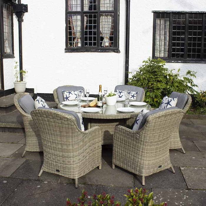 Full outdoor setup of the Wentworth 6 Seater Round Imperial Dining Set in a garden, showcasing the rattan chairs and round glass table arranged for an alfresco dining experience.