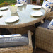 Outdoor dining setup with the Wentworth 6 Seater Round Imperial Dining Set, featuring rattan chairs with grey cushions and a round glass table set for a casual meal.