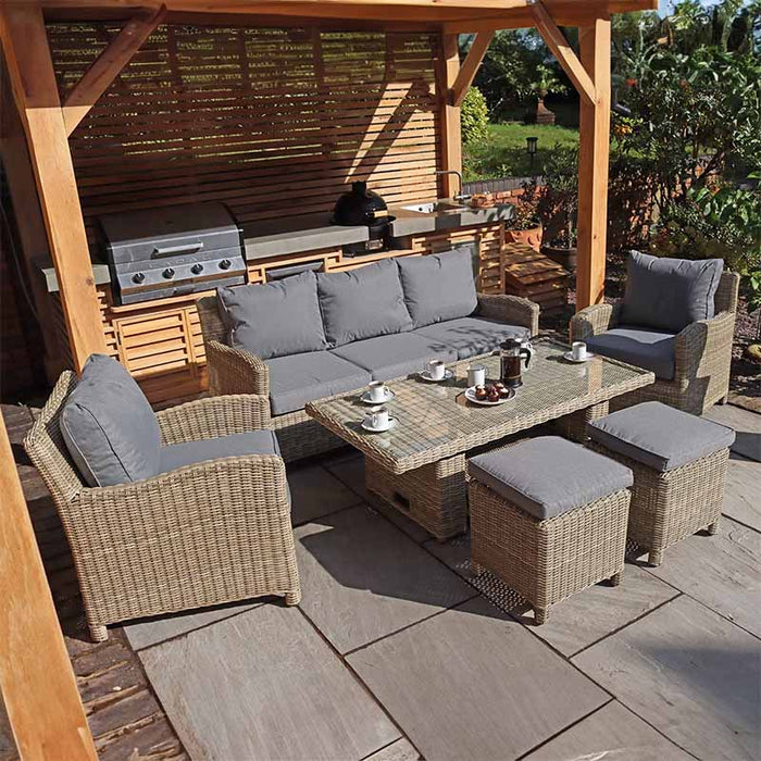 Wentworth Deluxe Sofa Dining Set arranged outdoors, featuring a comfortable seating area with a glass-top dining table and footstools.