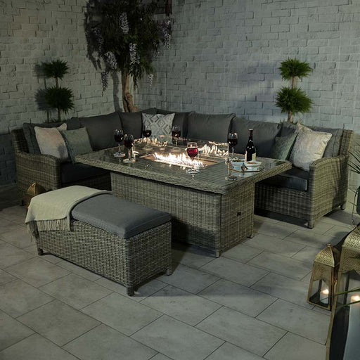 Wentworth Fire Pit Dining & Lounge Set with Rectangular Table at night, showcasing a stylish rattan corner sofa and matching bench, surrounding a rectangular table with a built-in fire pit, creating a cosy and inviting outdoor atmosphere.