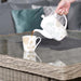 Pouring tea into a floral cup on the Wentworth Fire Pit Dining Set’s square table, highlighting a serene outdoor dining moment.