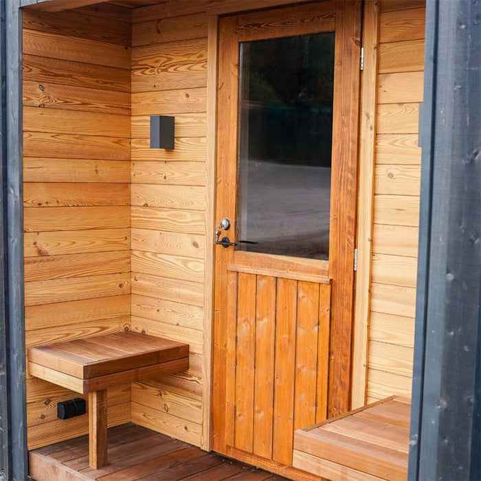 Woodnest Alice 2-3 Person Outdoor Sauna entrance with natural timber cladding, glazed wooden door and built-in porch seating.