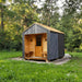 Woodnest Alice 2-3 Person Outdoor Sauna in a green forest setting with covered entrance, timber seating and dark diagonal cladding.