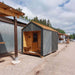 Woodnest Alice 2-3 Person Outdoor Sauna front view showing a covered timber porch, glazed entrance door and grey diagonal wood cladding.