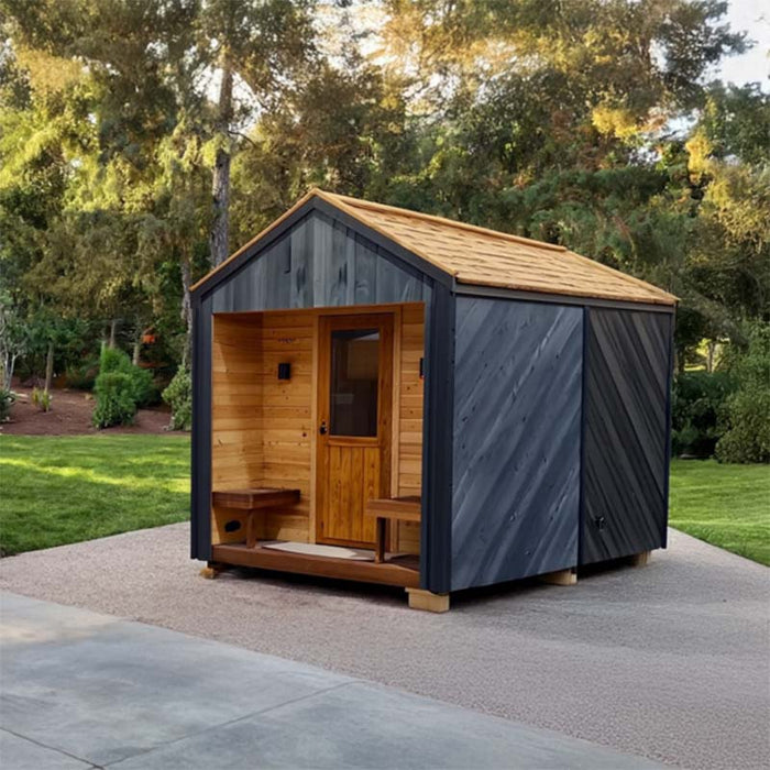 Woodnest Alice 2-3 Person Outdoor Sauna in a garden setting with dark timber exterior, wood-shingle roof and sheltered entrance.