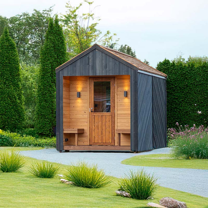 Woodnest Alice 2-3 Person Outdoor Sauna with covered timber entrance, glazed wooden door and dark cladding in a landscaped garden.