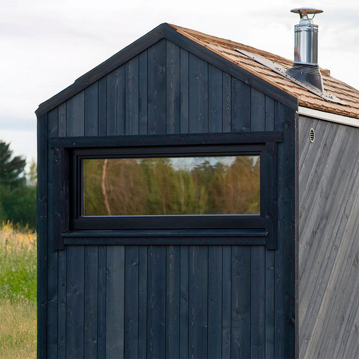 Woodnest Alice 2-3 Person Outdoor Sauna rear exterior featuring dark timber cladding, horizontal window and wood-shingle roof with chimney