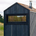 Woodnest Alice 2-3 Person Outdoor Sauna rear exterior featuring dark timber cladding, horizontal window and wood-shingle roof with chimney