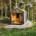 Woodnest Alice 2-3 Person Outdoor Sauna surrounded by woodland, featuring a natural timber porch, glazed door and grey wood exterior.