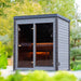 Woodnest Lucia 2 Person Outdoor Sauna with contemporary grey timber cladding, glazed front and warmly illuminated interior surrounded by greenery.