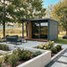 Woodnest Nora 3-4 Person Outdoor Sauna with grey timber cladding, covered terrace and large glazed entrance in a landscaped garden.